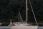 Beneteau 393 - 2003 Beneteau 393 sailboat anchored on a calm lake with forested background.