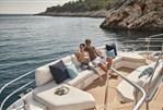 Prestige M8 - Couple relaxing on a Prestige M8 yacht, 2025 model, near a scenic coastline.