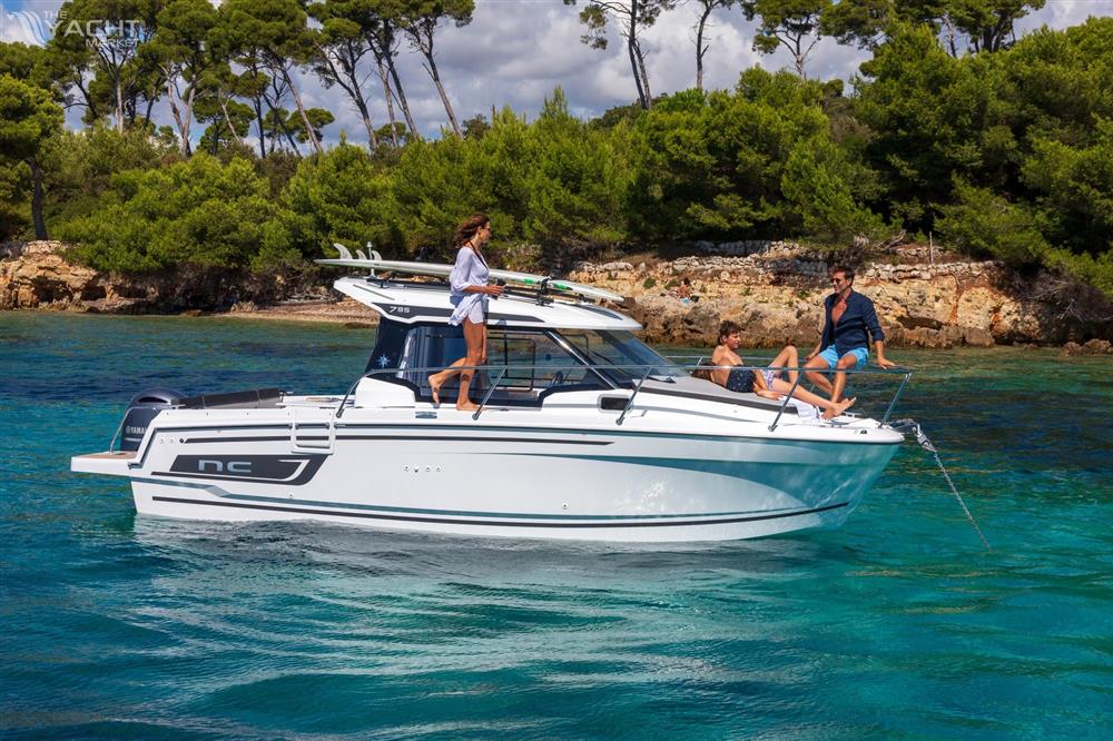 Jeanneau NC 795 S2 - 2025 Jeanneau NC 795 S2 boat cruising in clear blue water near a forested shoreline.