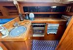 Moody 34 - 1985 Moody 34 yacht kitchen with wooden cabinetry, sink, stove, and nautical-themed flooring.
