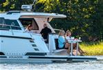 Aquador 300 HT - Aquador 300 HT 2026 yacht with people dining on deck, surrounded by lush greenery.